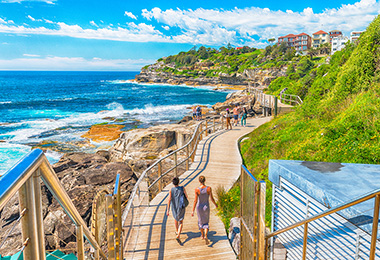 一對情侶走在邦迪海灘的棧道上前進，右邊是綠色山坡左邊是藍色的海