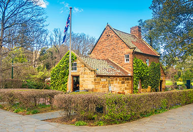 磚紅色的庫克船長的小屋，前方有澳洲國旗