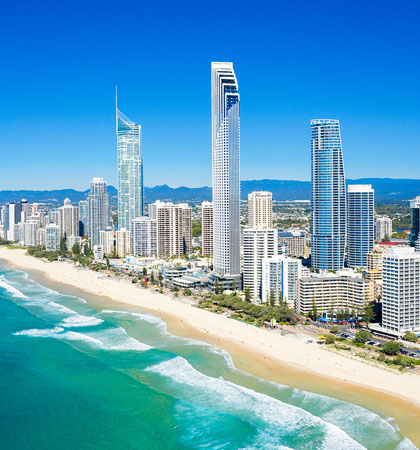 左邊是白色的浪花打在白色的沙灘上，右邊是一整排現代高樓大廈