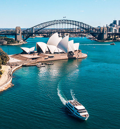 雪梨歌劇院搭配著背後的雪梨大橋，前方海灣有一艘船行駛過